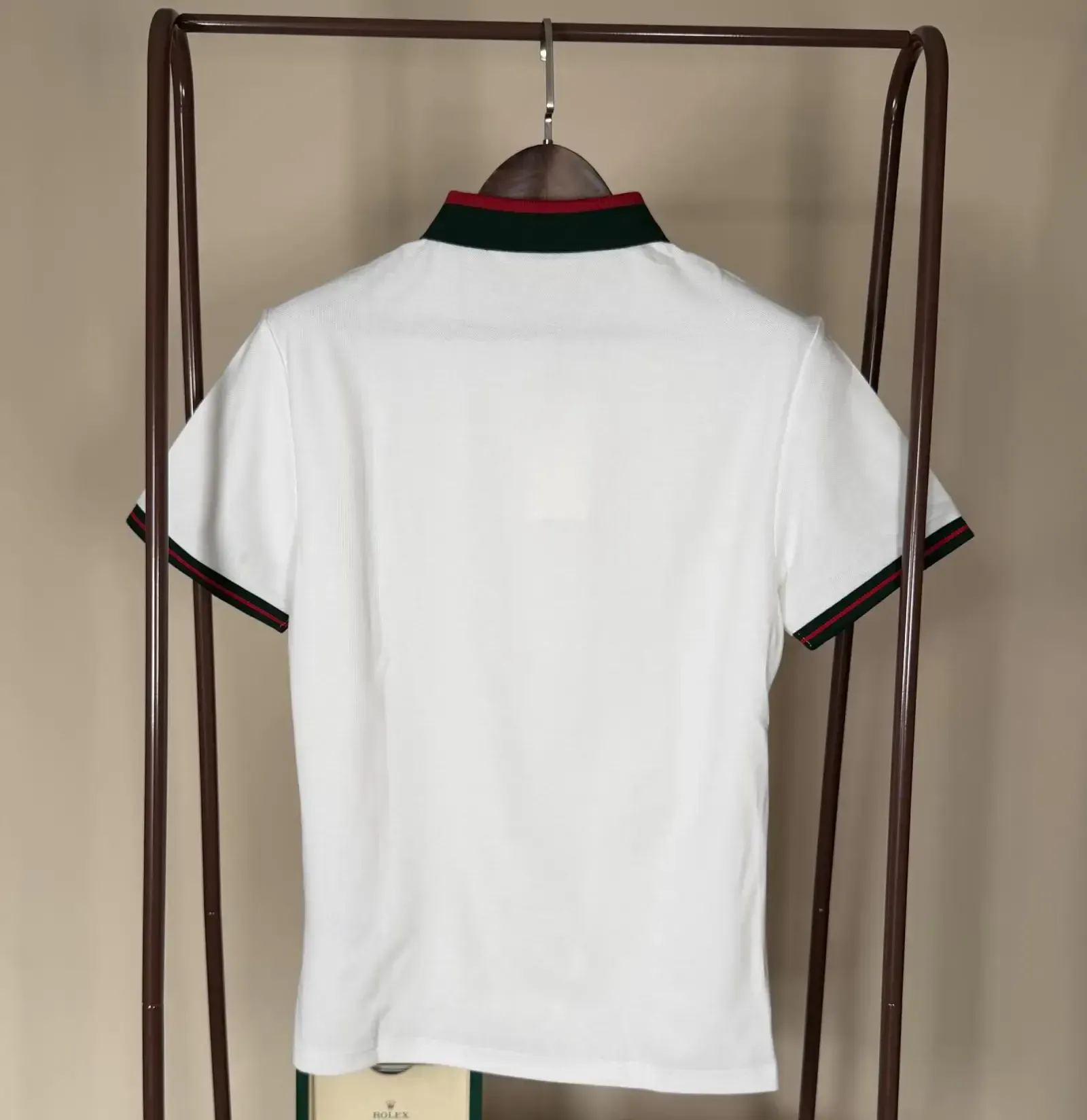 White polo shirt with green and red collar trim hanging on a clothing rack.