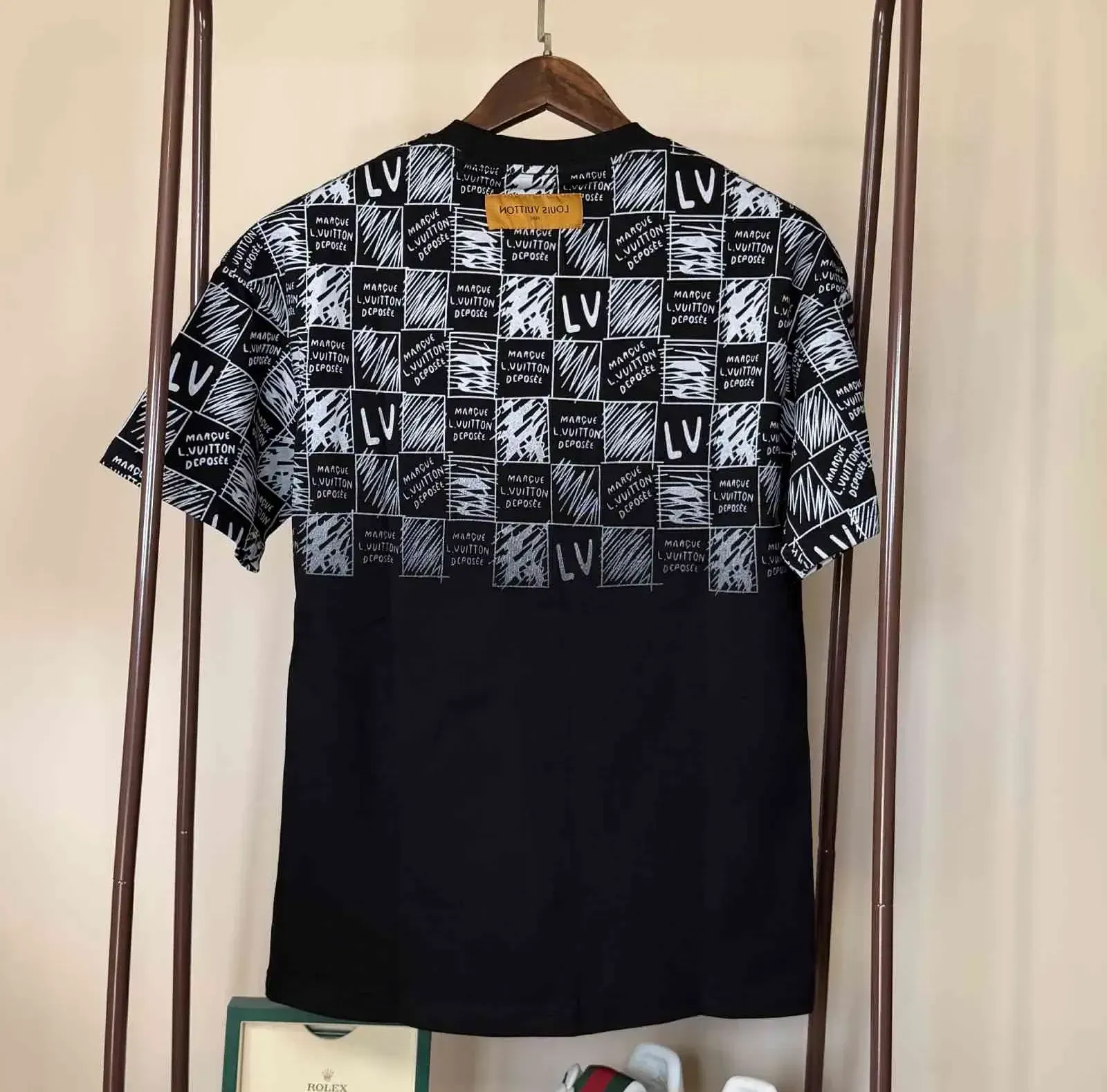 Black and white LVE t-shirt with checkered print on top half, hanging on a rack.