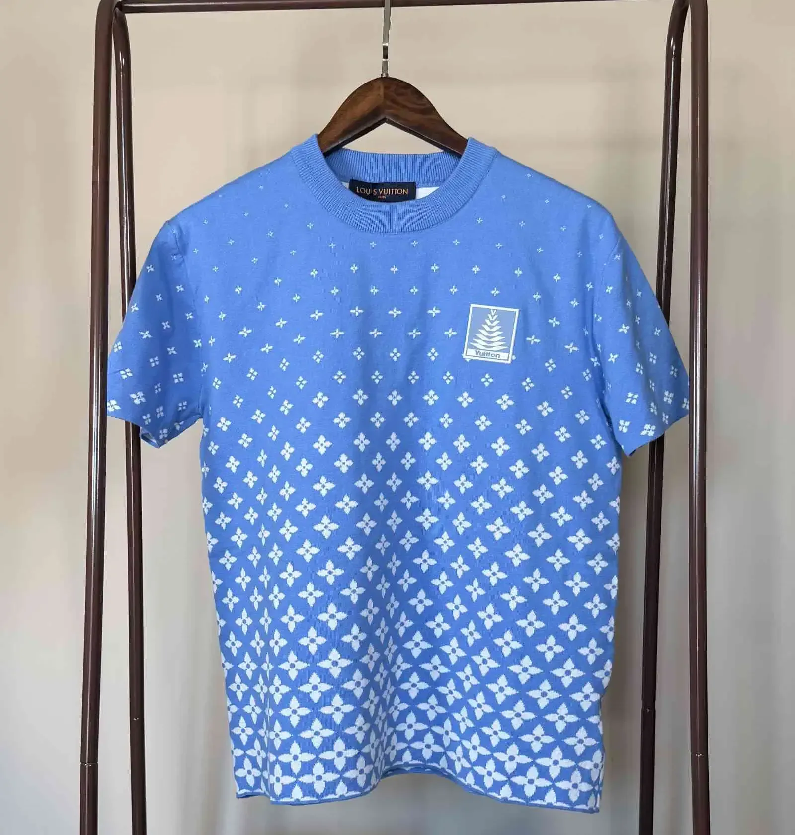 Blue patterned short-sleeve shirt with a small chest logo, hanging on a clothing rack.