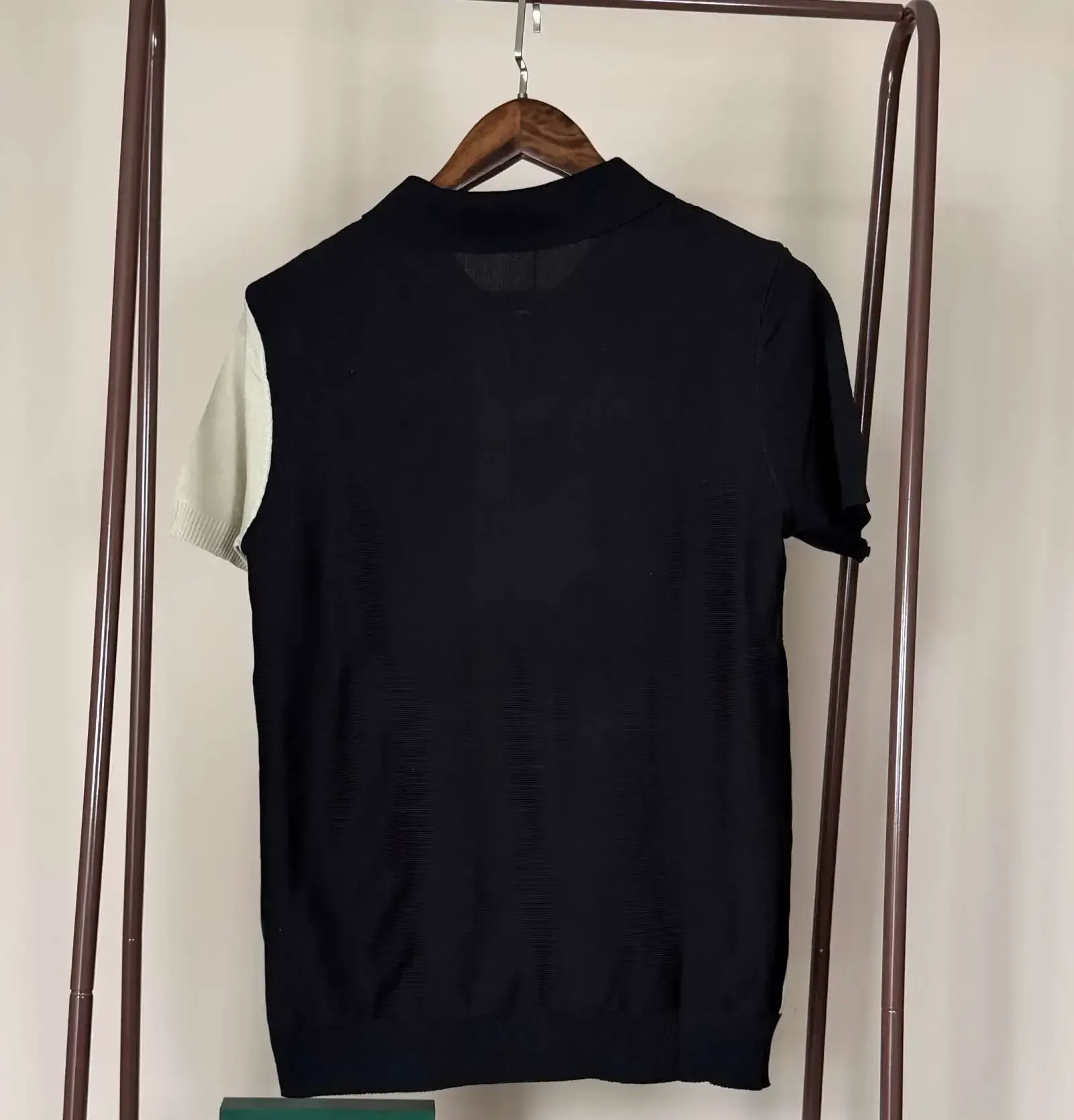 Black, green, and cream striped polo shirt with LVE, hanging on a brown rack.
