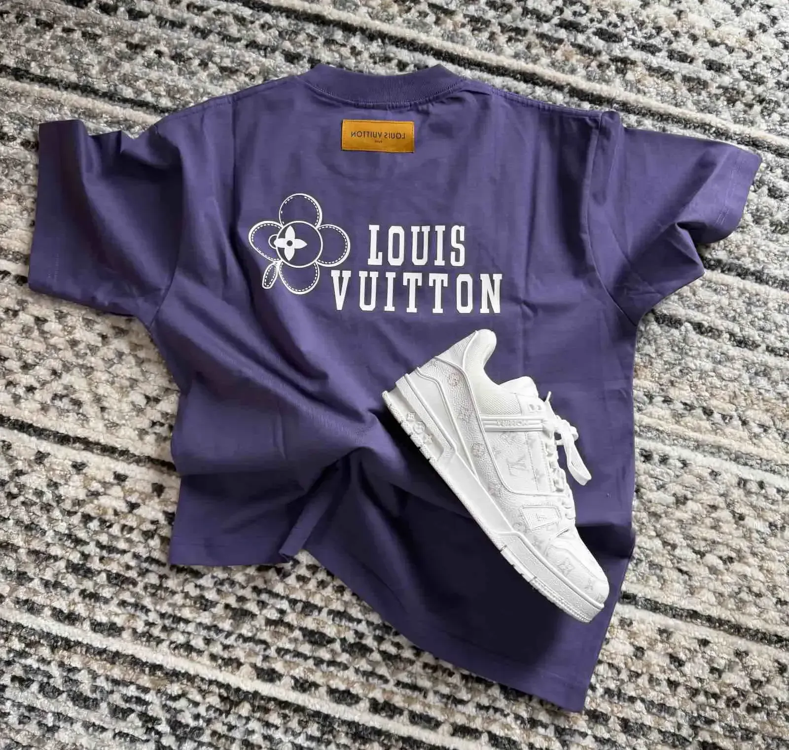 Purple LVE T-shirt and white LV sneakers on a textured gray surface.