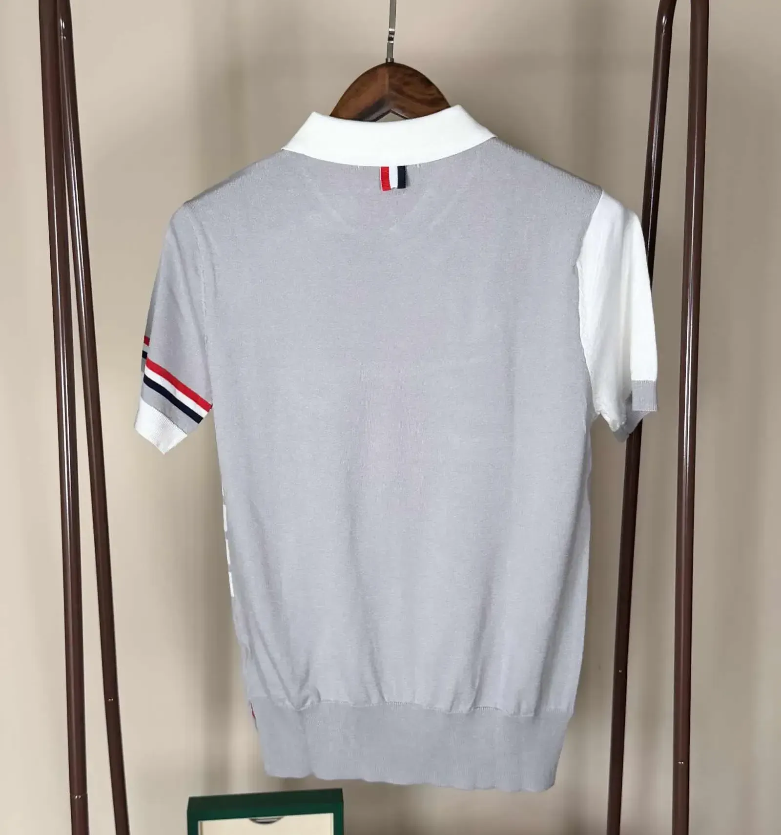 Gray and white polo shirt with three-stripe detail on the sleeve and front, hanging on a clothing rack.