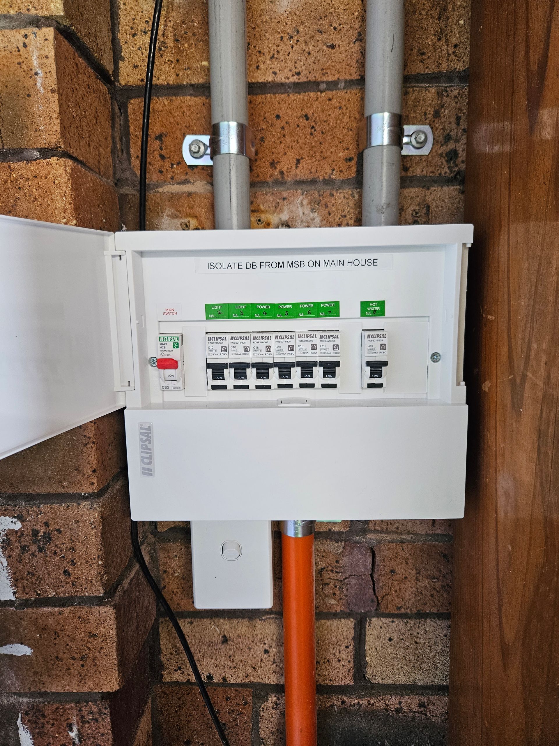 A white box is sitting on a brick wall next to a pipe.