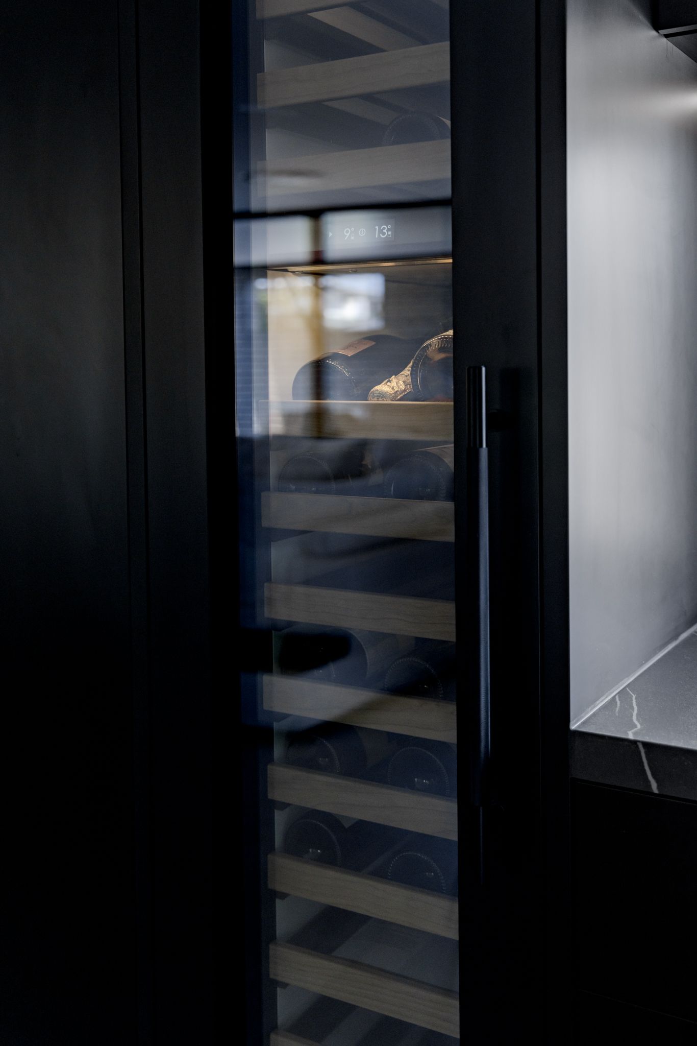 A contemporary all-black kitchen featuring an integrated wine fridge.