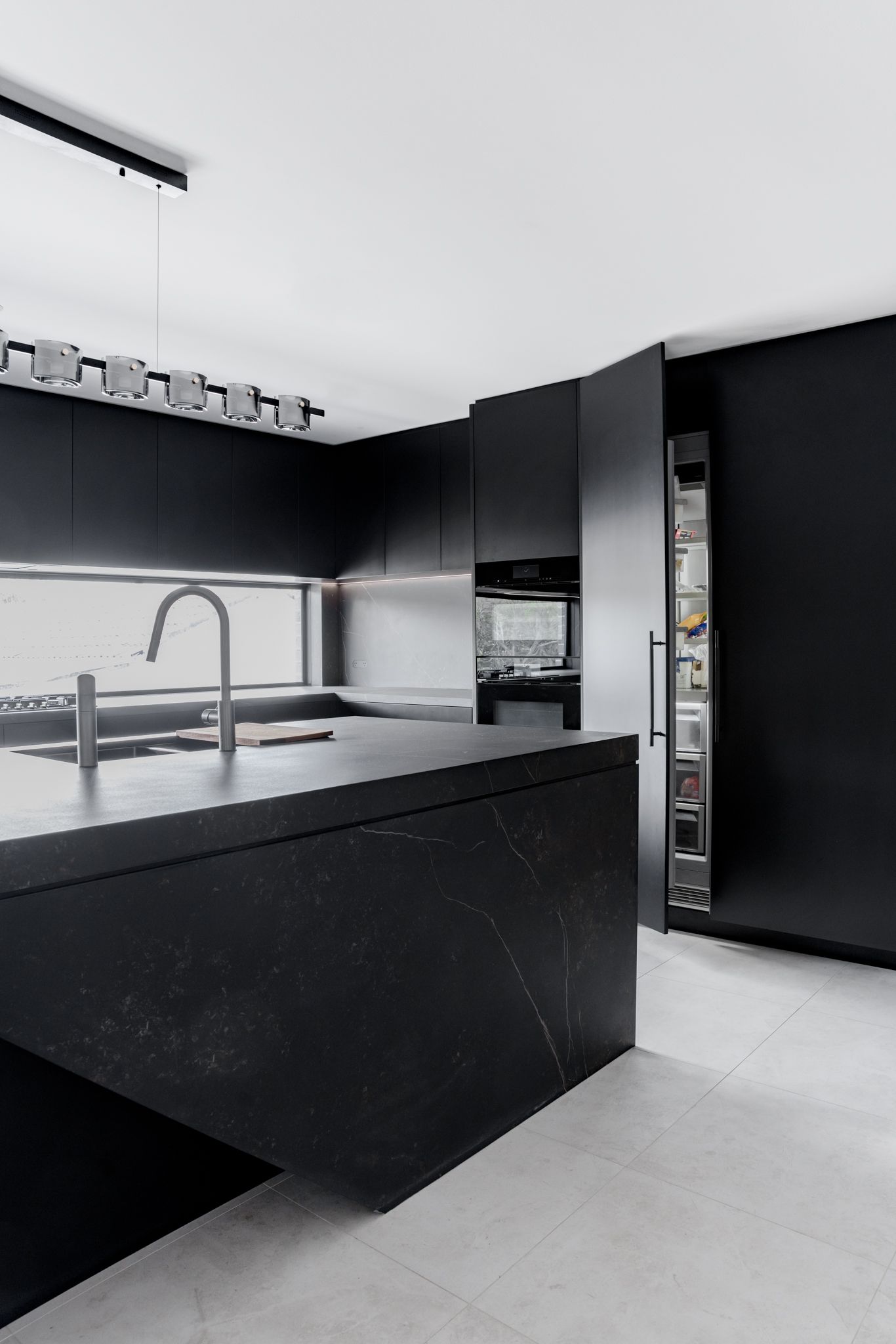 A modern all-black sleek kitchen with matte joinery and black veined stone countertops.