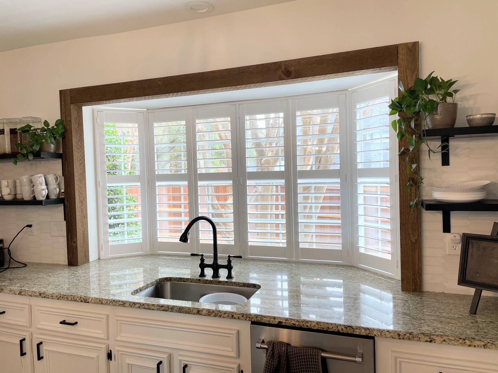 A kitchen with a sink and a large window with shutters.