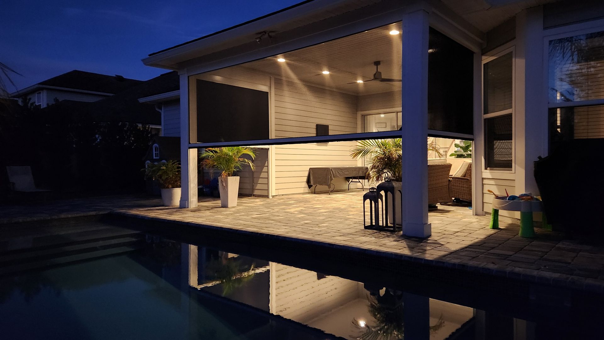 A house with a covered patio and a swimming pool at night.