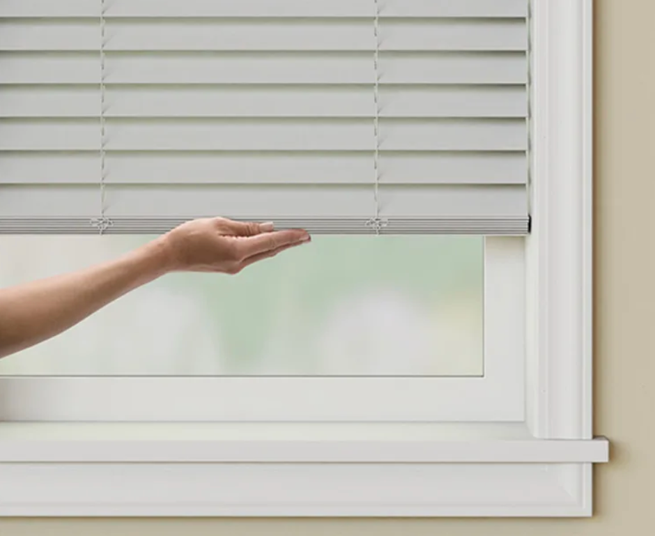 A person is holding a blind in a window.