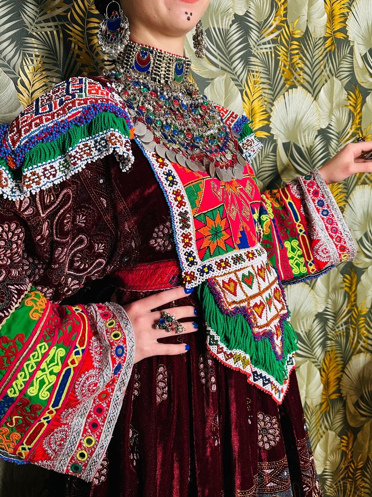 Eine Frau in einem bunten Kleid und einer Jacke steht vor einer geblümten Tapete.