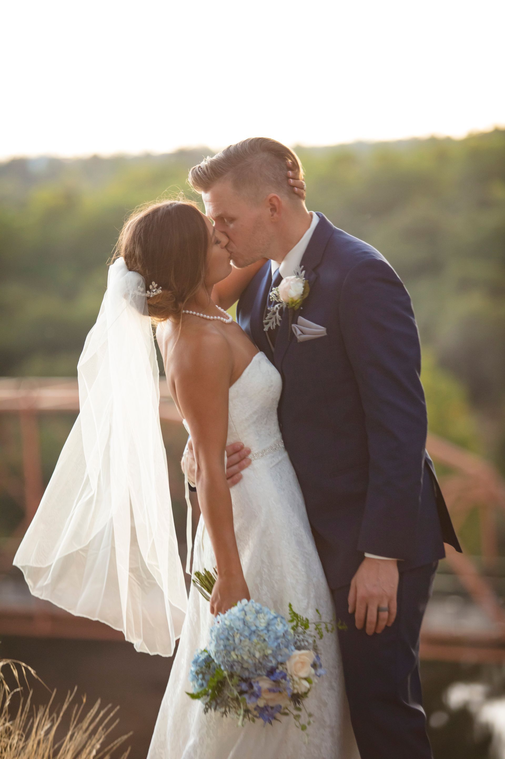 Eine Braut und ein Bräutigam küssen sich vor einer Brücke.