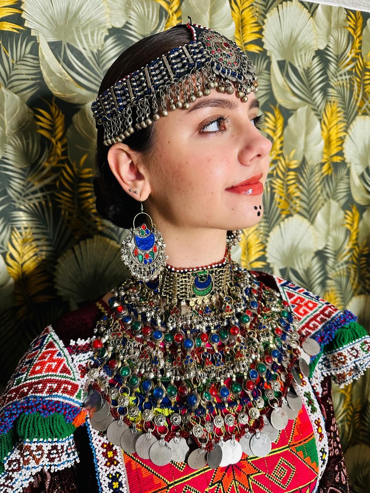 Eine Frau mit Stirnband und Ohrringen steht vor einer Blumentapete.
