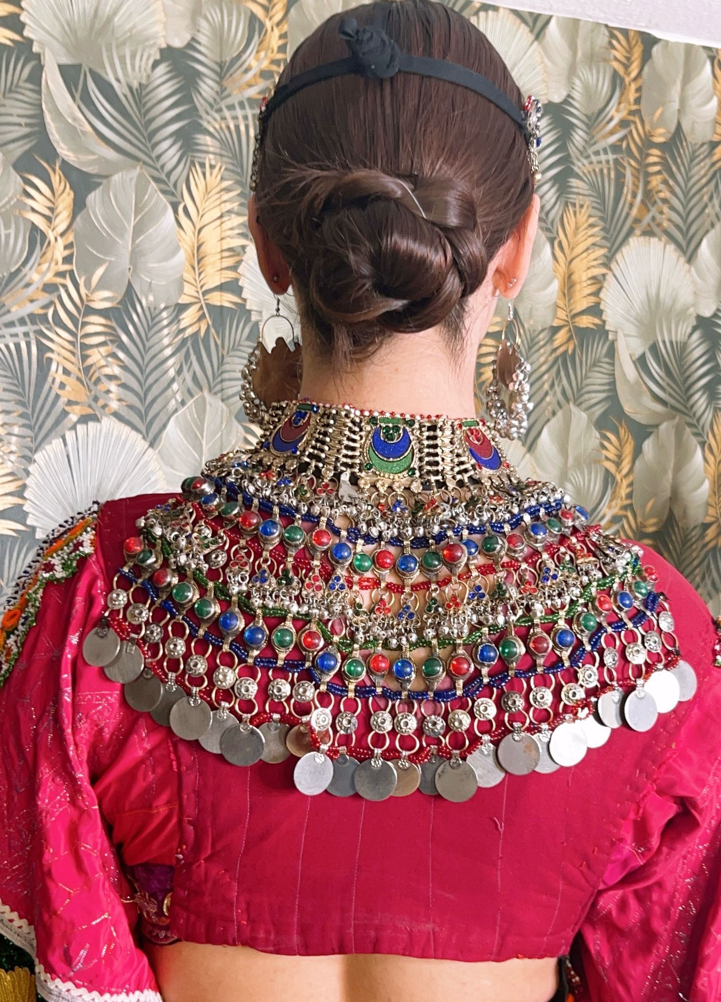 Der Rücken einer Frau, die eine rote Bluse mit Halskette und Ohrringen trägt.