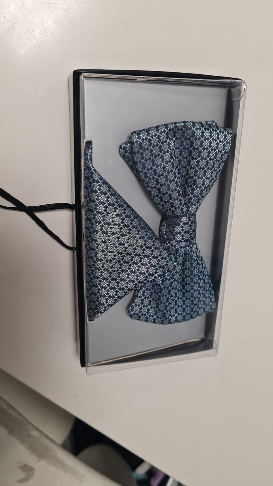 Eine Fliege und ein Einstecktuch liegen in einer Schachtel auf einem Tisch.