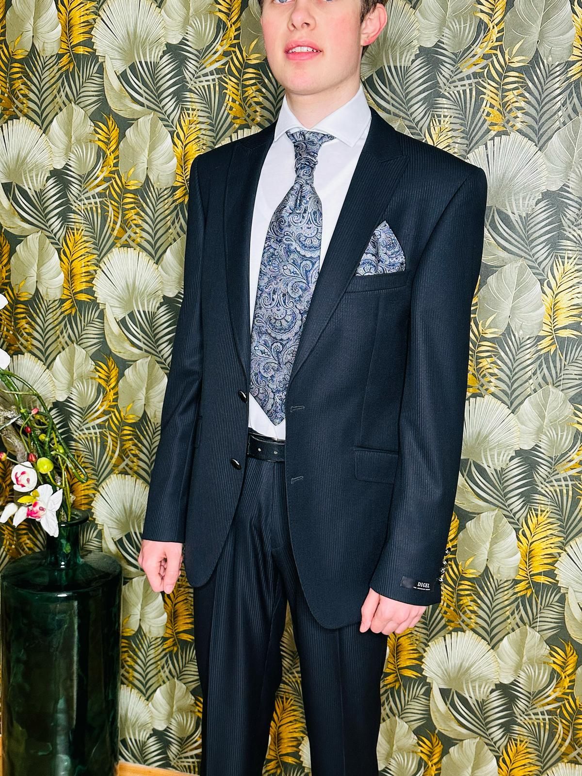 Ein junger Mann in Anzug und Krawatte steht vor einer Blumentapete.