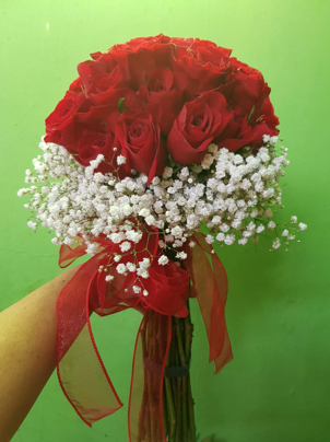 Una persona sostiene un ramo de rosas rojas y flores de aliento de bebé.