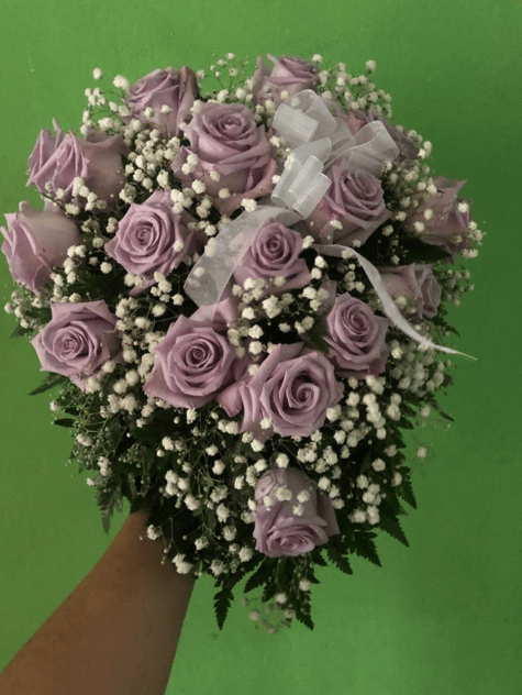 Una persona sostiene un ramo de rosas moradas y flores de aliento del bebé.