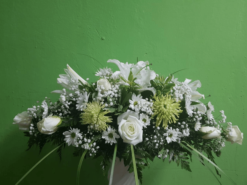 Un ramo de flores blancas está sobre una mesa frente a una pared verde.