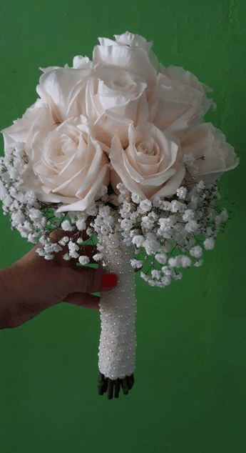 Una persona sostiene un ramo de rosas blancas y flores de bebé.