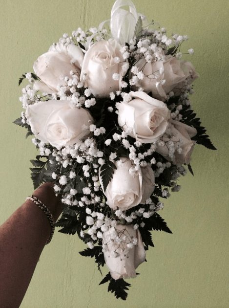 Una persona sostiene un ramo de rosas blancas y flores de aliento del bebé.