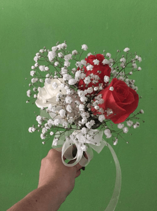 Una persona sostiene un ramo de rosas rojas y blancas y flores de bebé.