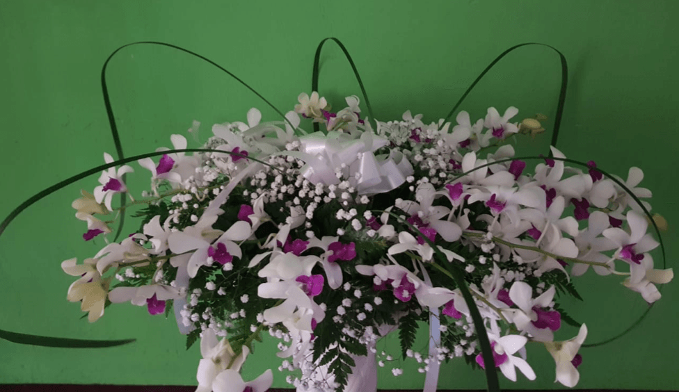 Un jarrón lleno de flores blancas y moradas contra una pared verde.