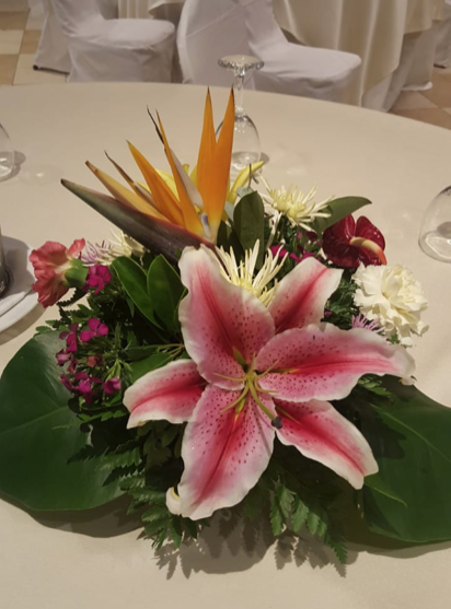 Un lirio rosa está rodeado de otras flores sobre una mesa.