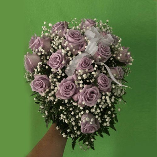 Una persona sostiene un ramo de rosas moradas y flores de aliento del bebé.