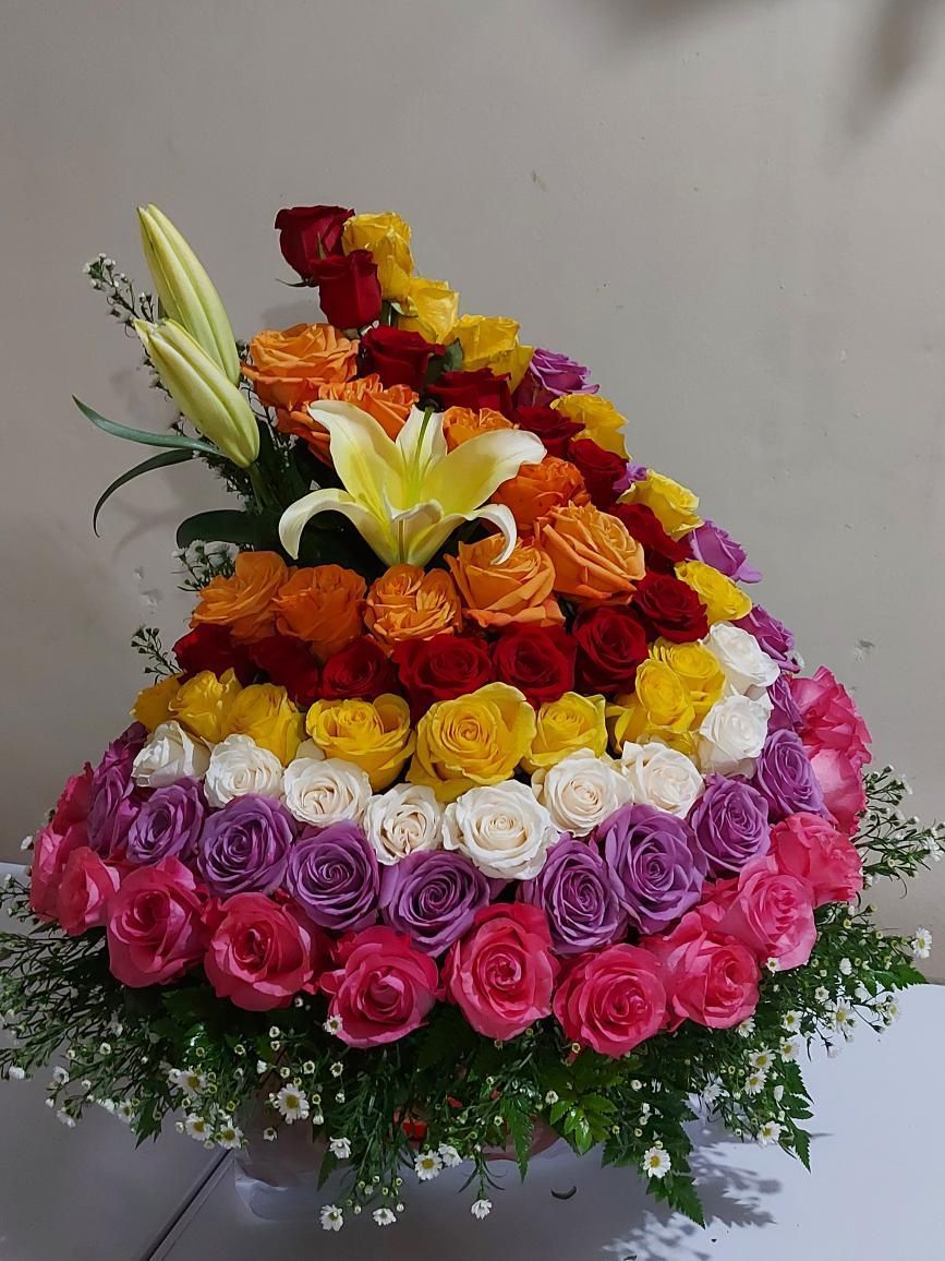 Un jarrón lleno de rosas y lirios de diferentes colores.