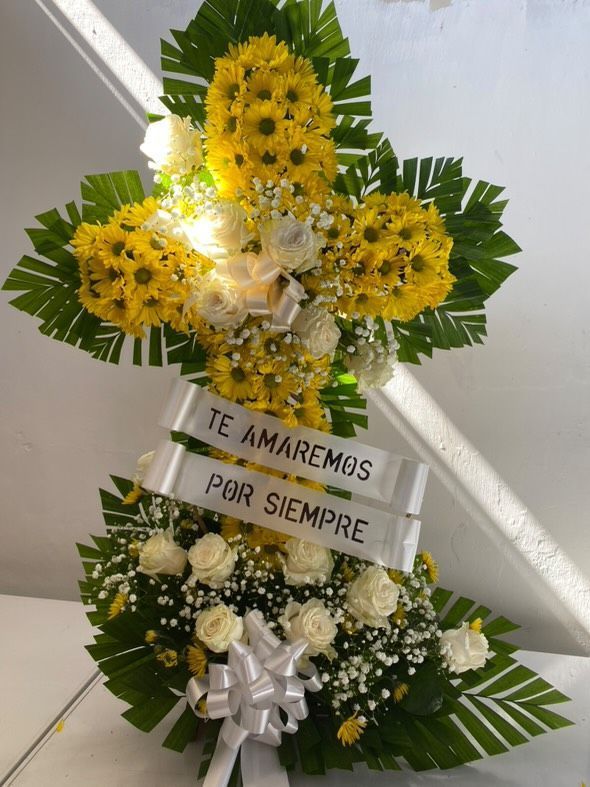 Una cruz hecha de flores amarillas y blancas con una cinta que dice te amaremos por siempre