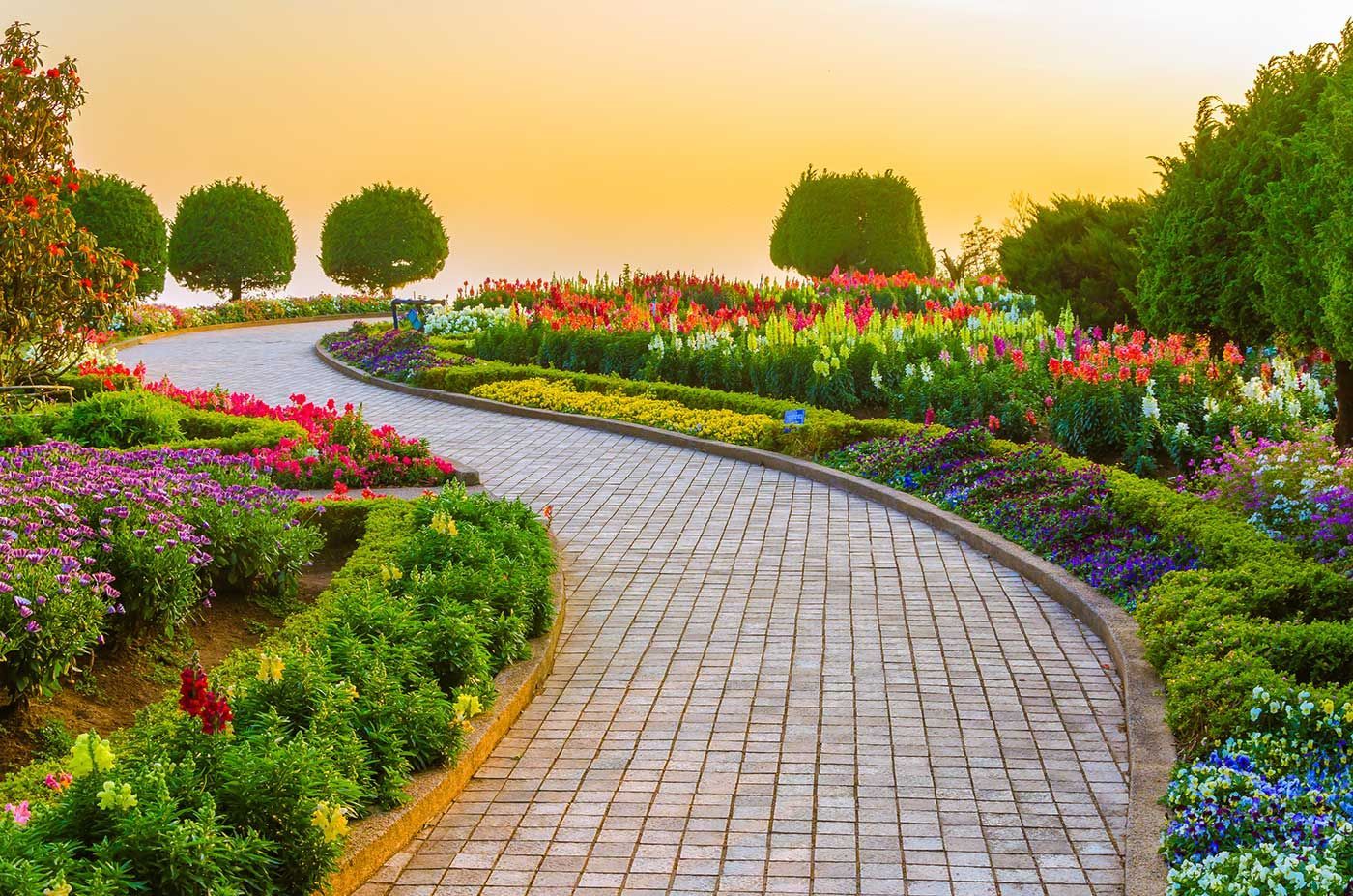 A brick walkway surrounded by flowers and trees in a garden.
