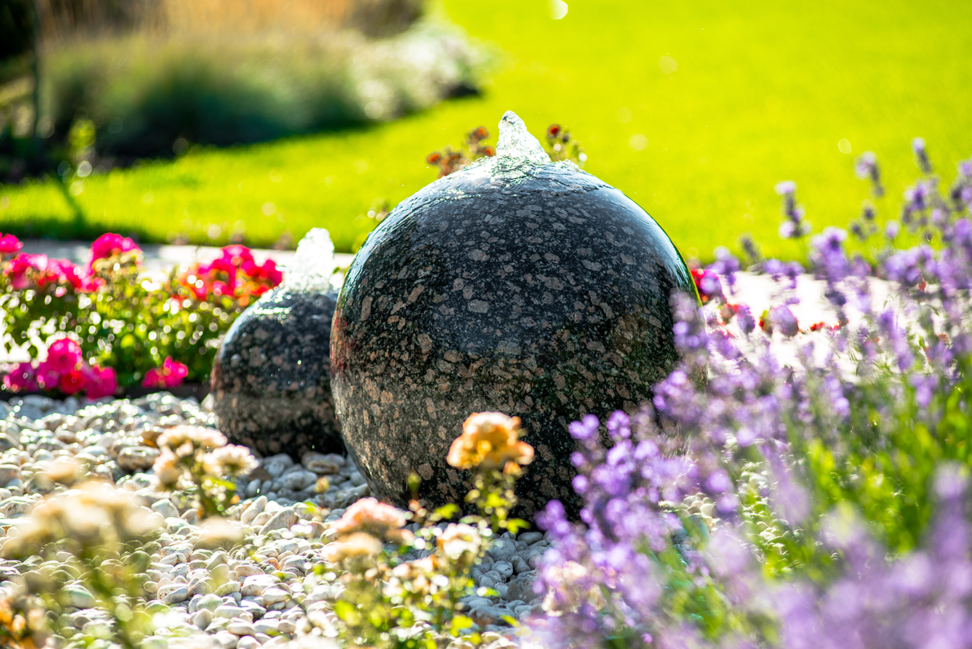 A fountain in a garden surrounded by purple flowers and rocks.