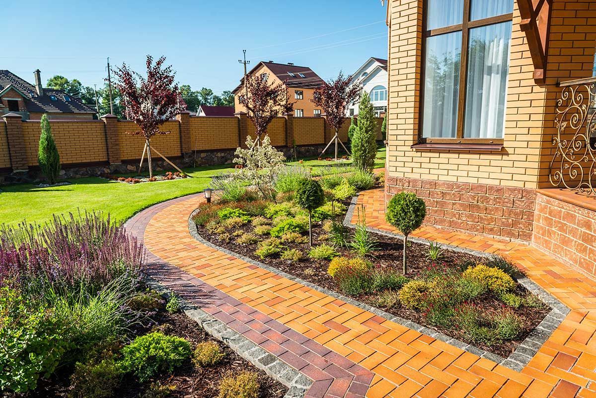 A brick walkway leading to a house with a garden in front of it.