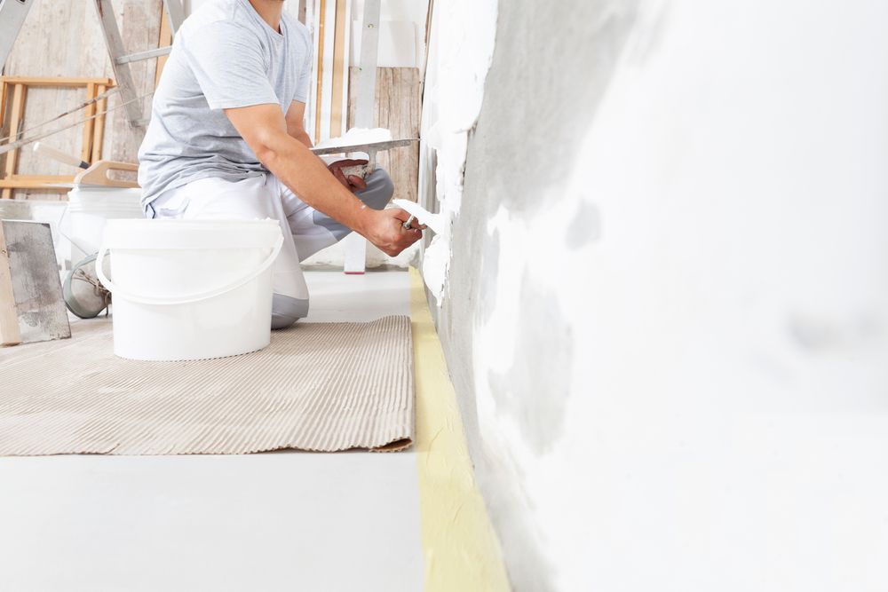 A man is kneeling on the floor painting a wall.