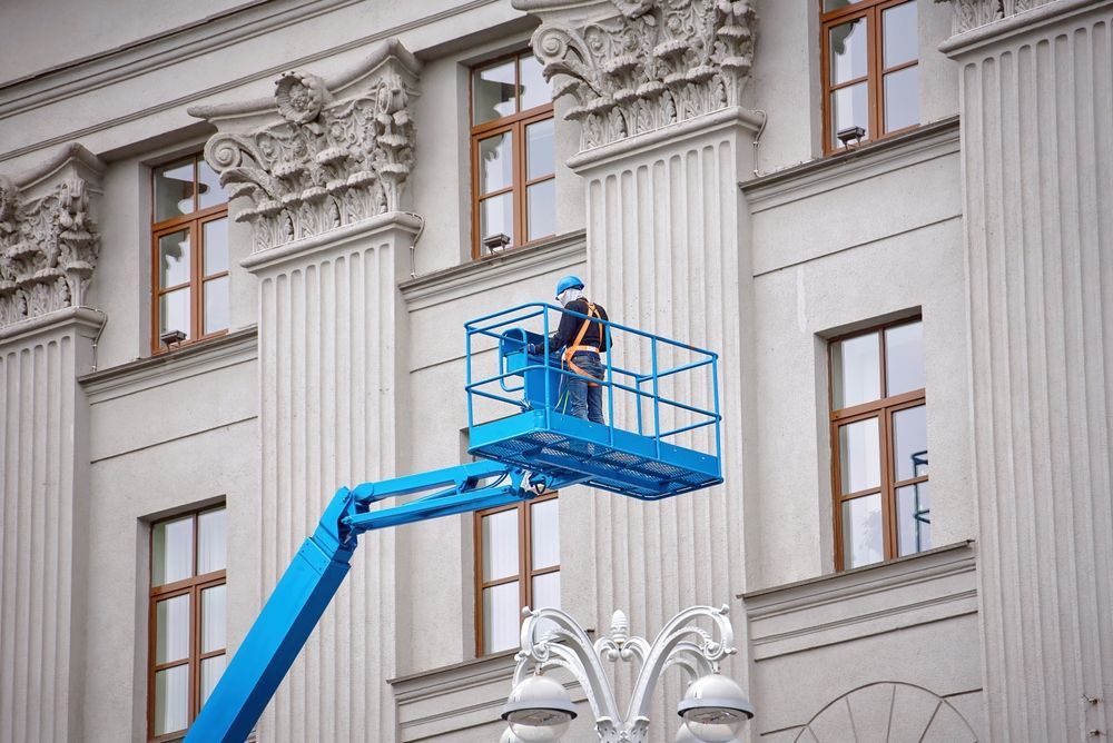A man is standing on a lift in front of a building.