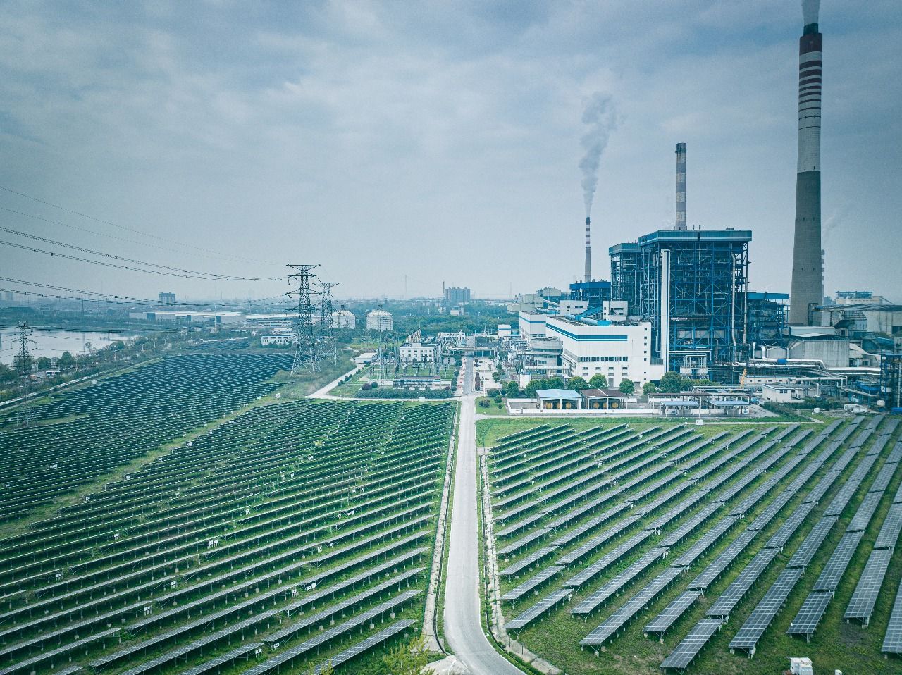 Solar panels and a power plant emitting smoke, in an industrial area.