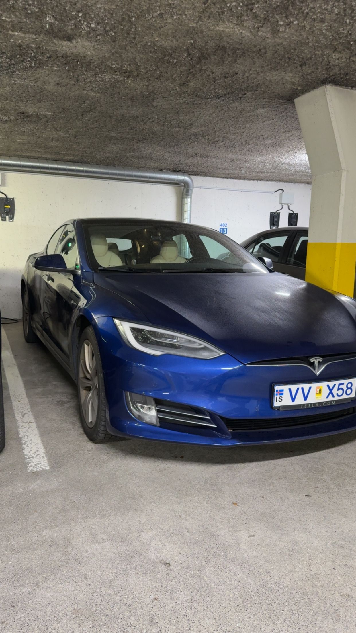 Blue Tesla sedan parked in an underground garage with charging stations.