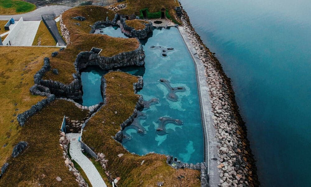An aerial view of a natural-looking swimming pool carved into the cliffside with clear turquoise water next to the ocean.