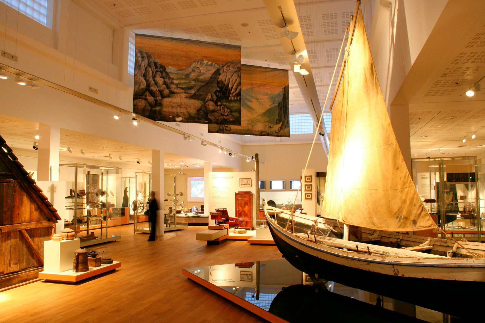 Museum exhibit hall with sailboat and landscape paintings.