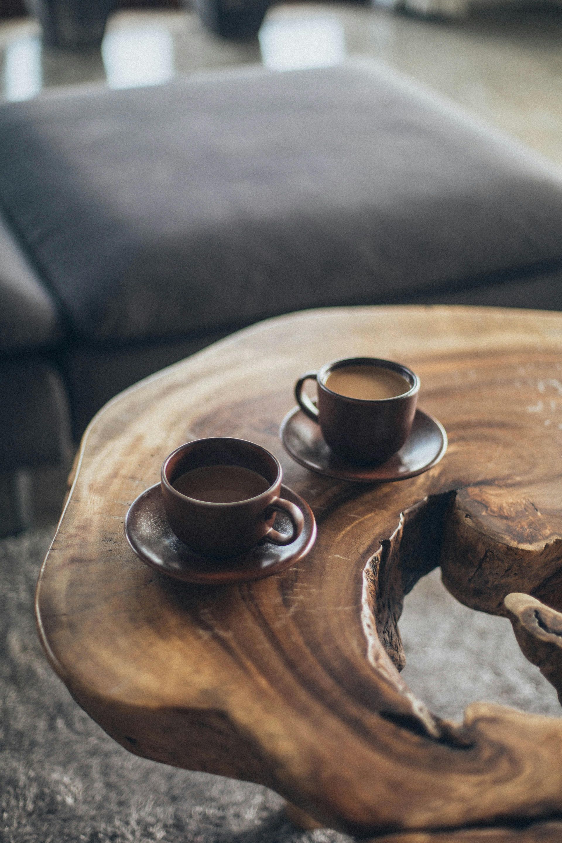 Two cups of coffee on saucers sit on a rustic wooden coffee table.