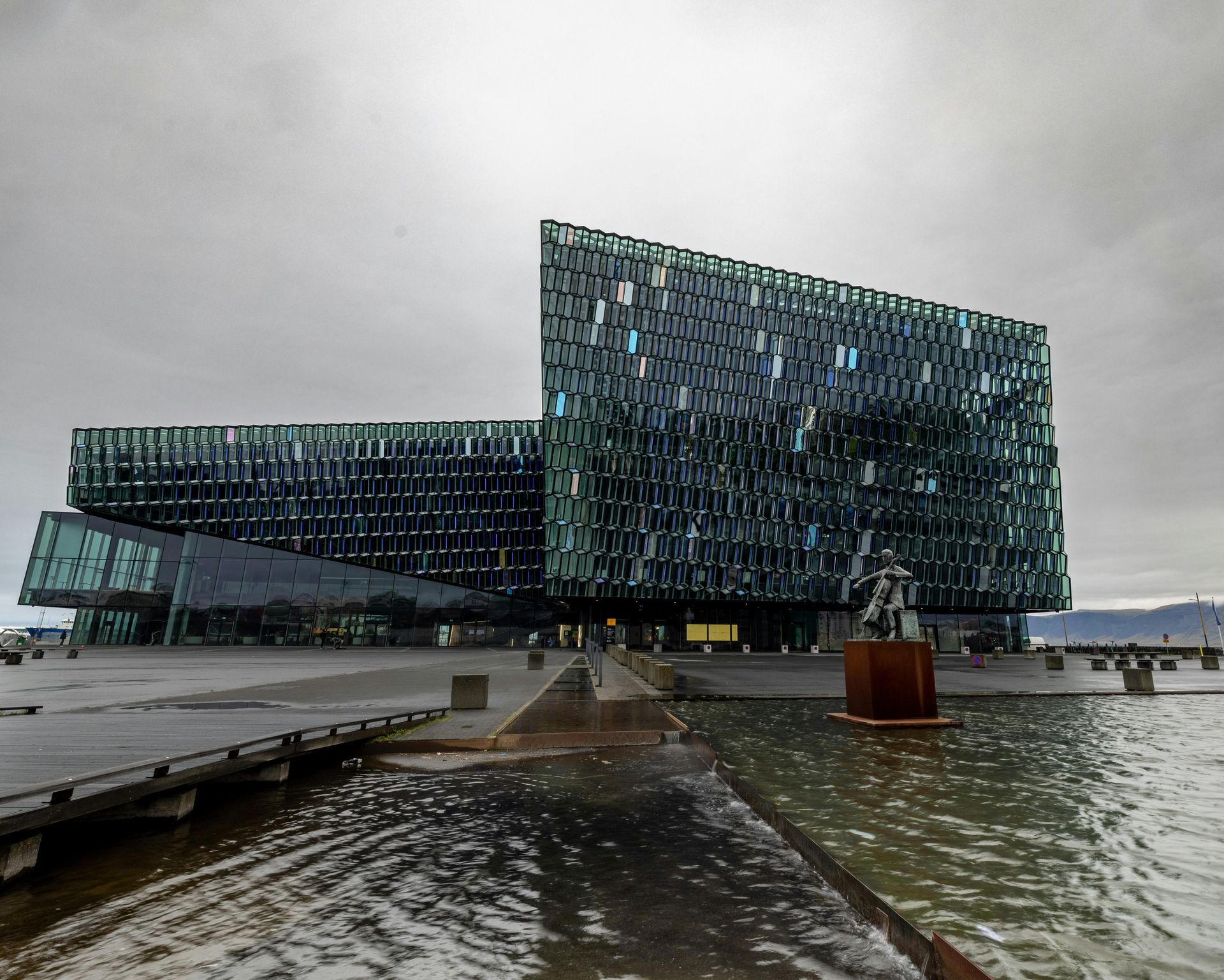 Harpa Concert Hall in Reykjavik, Iceland, with glass facade reflecting cloudy sky, overlooking water.