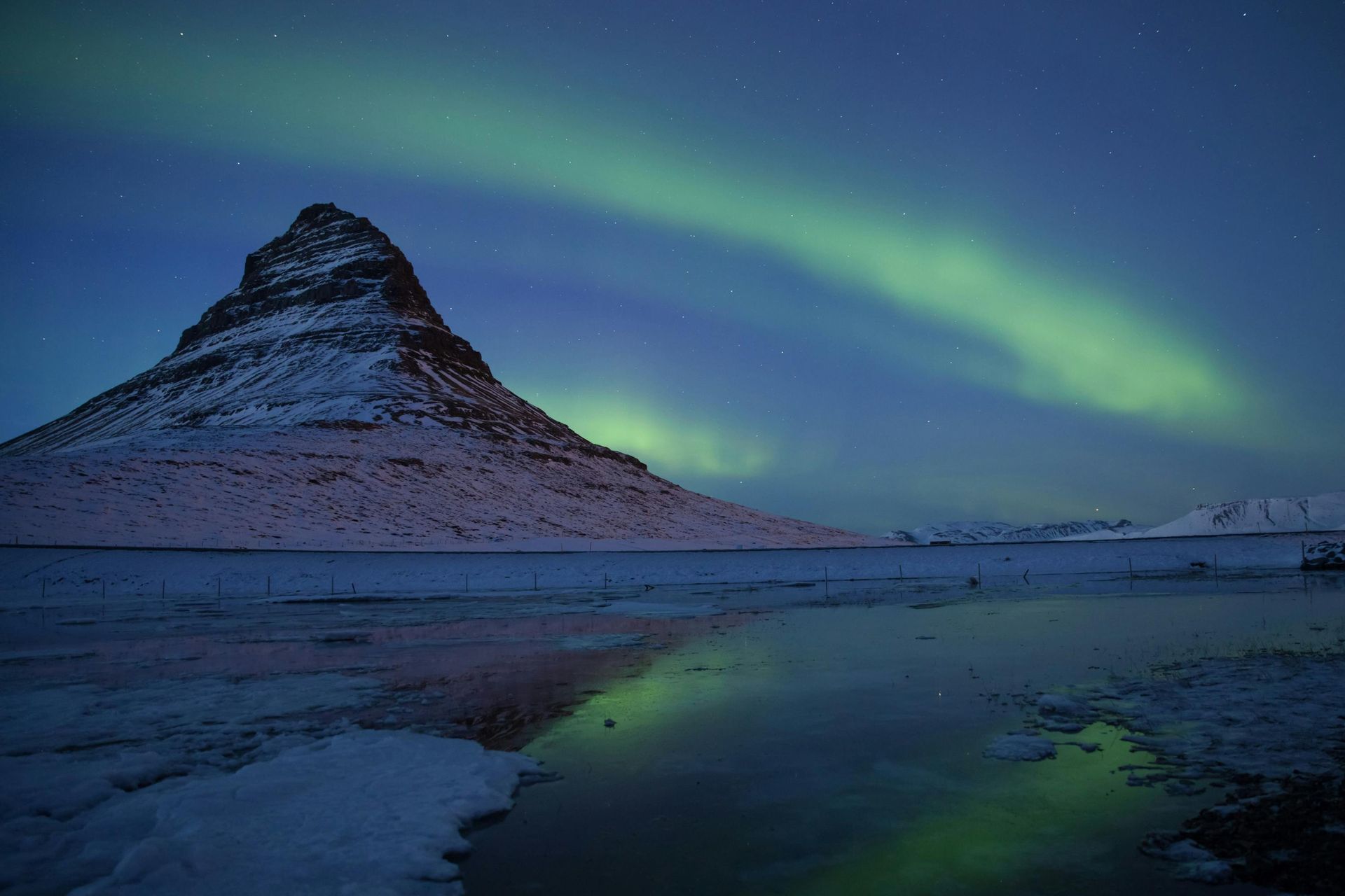 Northern lights above Kirkjufell mountain, Iceland; green and blue hues reflect in water.
