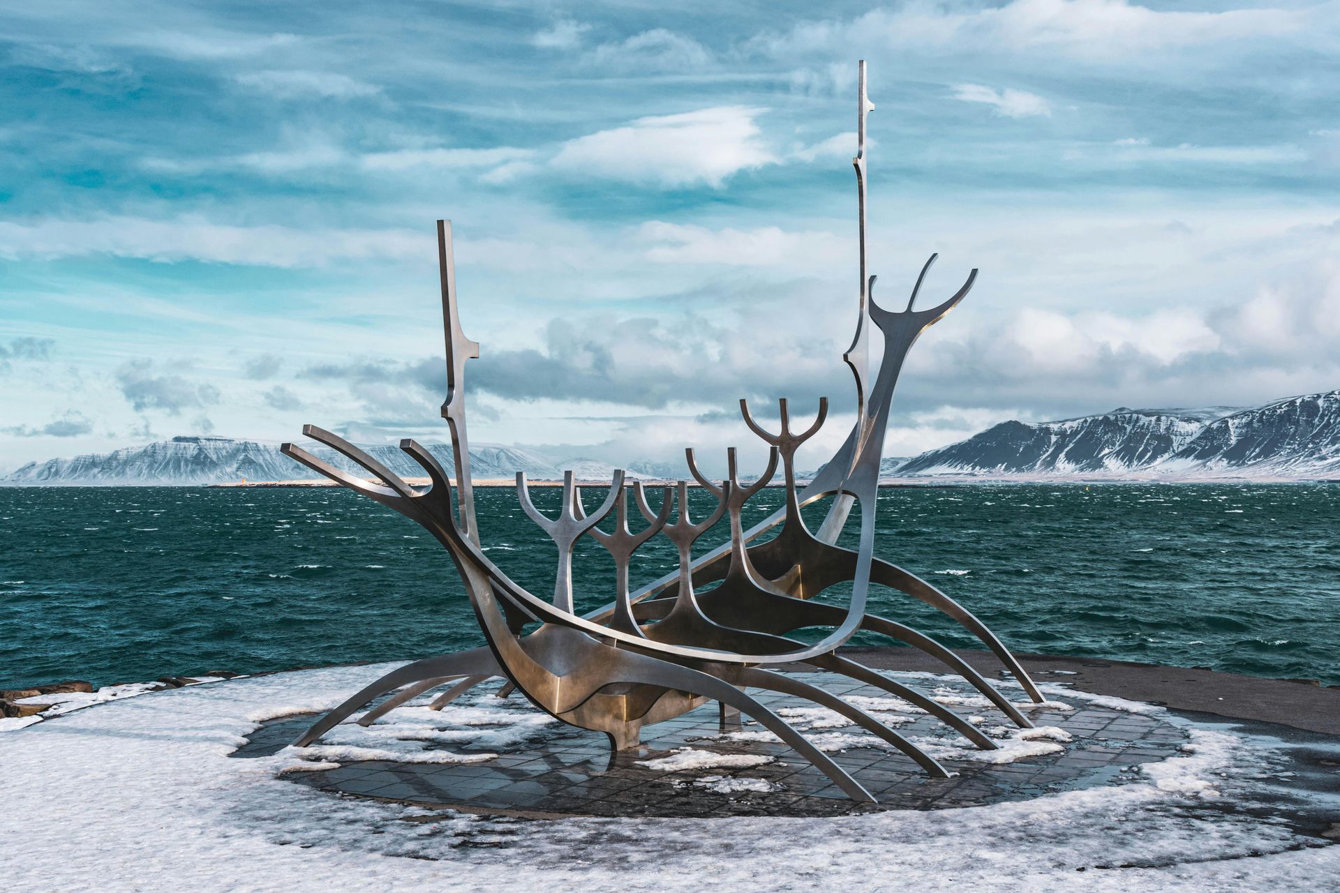 Sculpture of a Viking ship on a snowy shore, overlooking the ocean with mountains in the background.