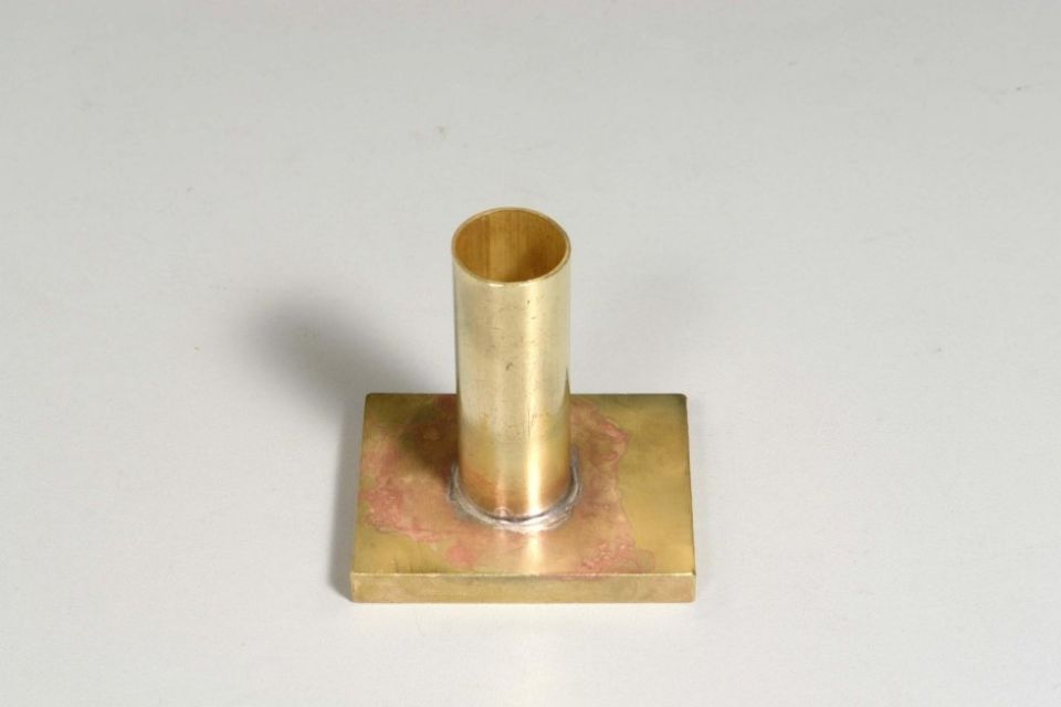 Un tubo di ottone è appoggiato sopra un pezzo quadrato di metallo.