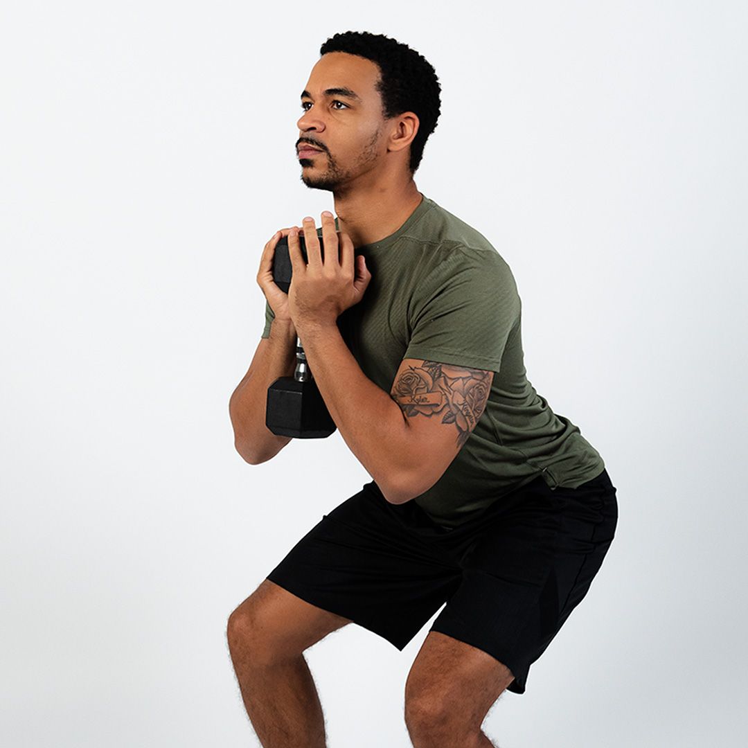 A man is squatting down while holding a dumbbell in his hands.