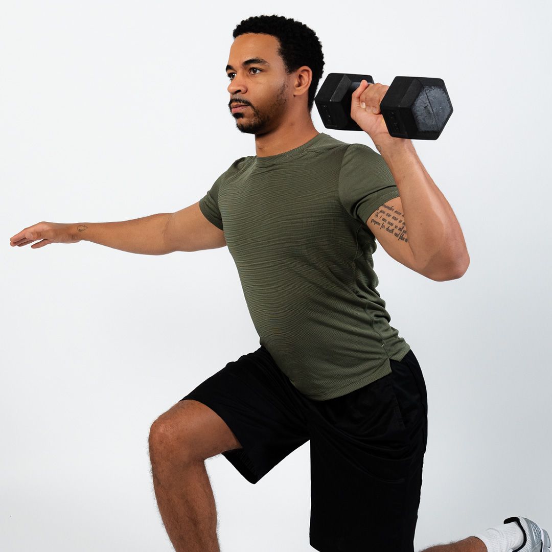 A man in a green shirt is holding a dumbbell over his shoulder