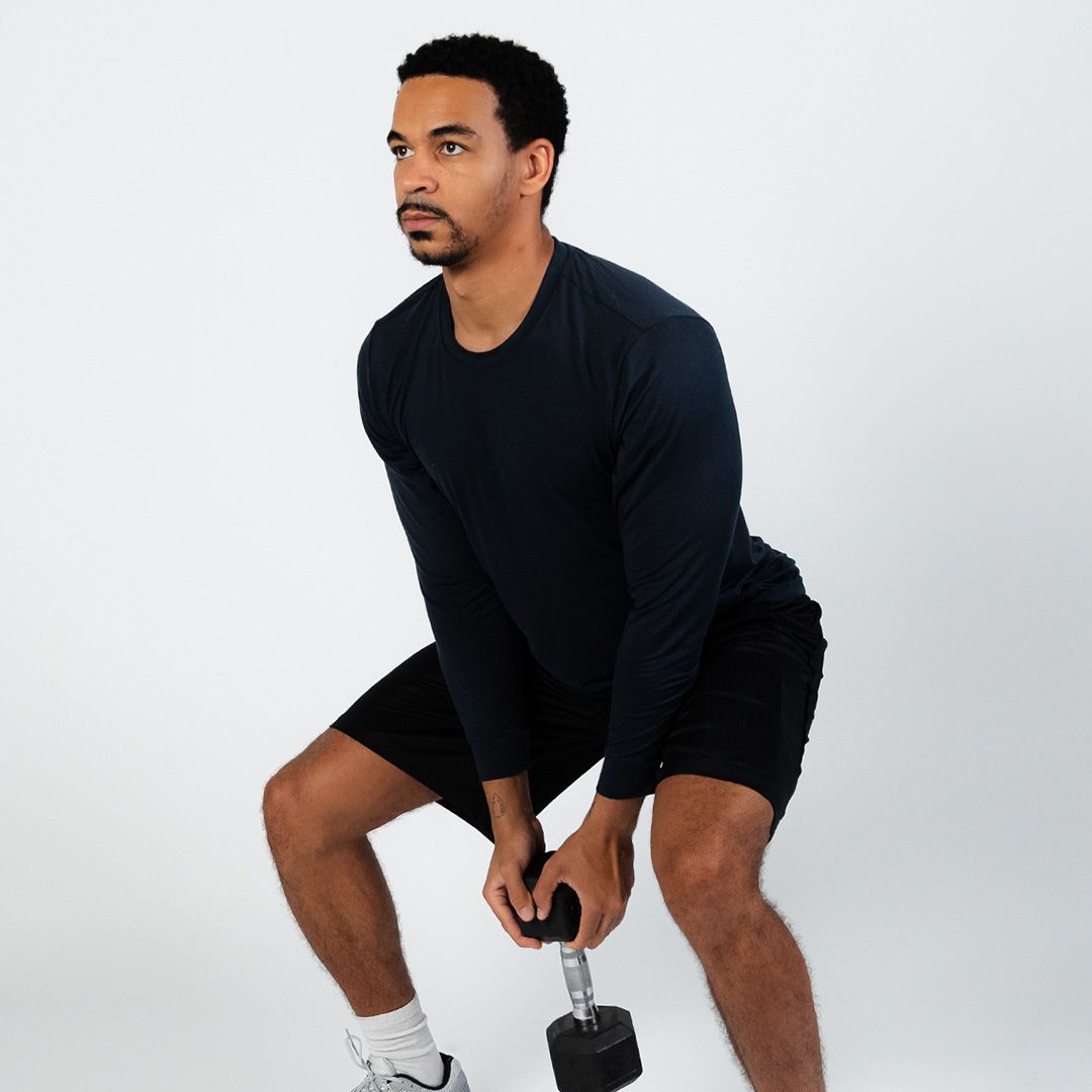 A man squatting down holding a dumbbell in his hands