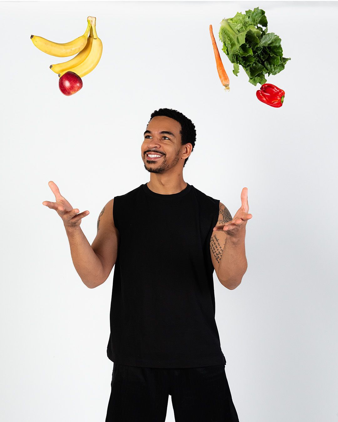 A man is juggling fruits and vegetables in the air.