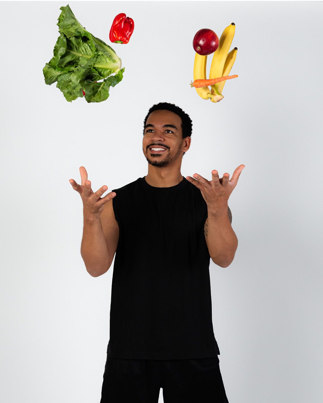 A man in a black shirt is juggling fruits and vegetables.