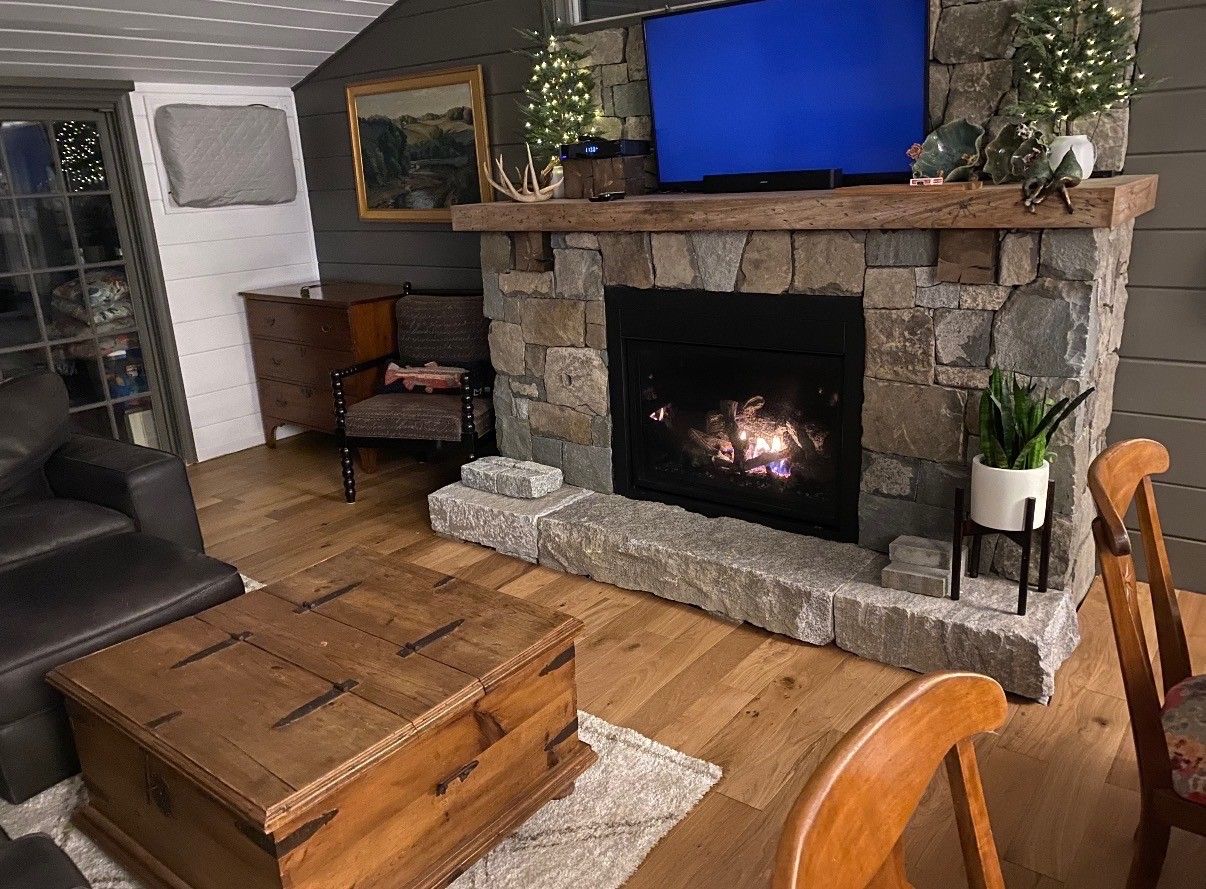 A living room features a stone fireplace with a glowing fire, a large wooden coffee table, and a leather armchair.