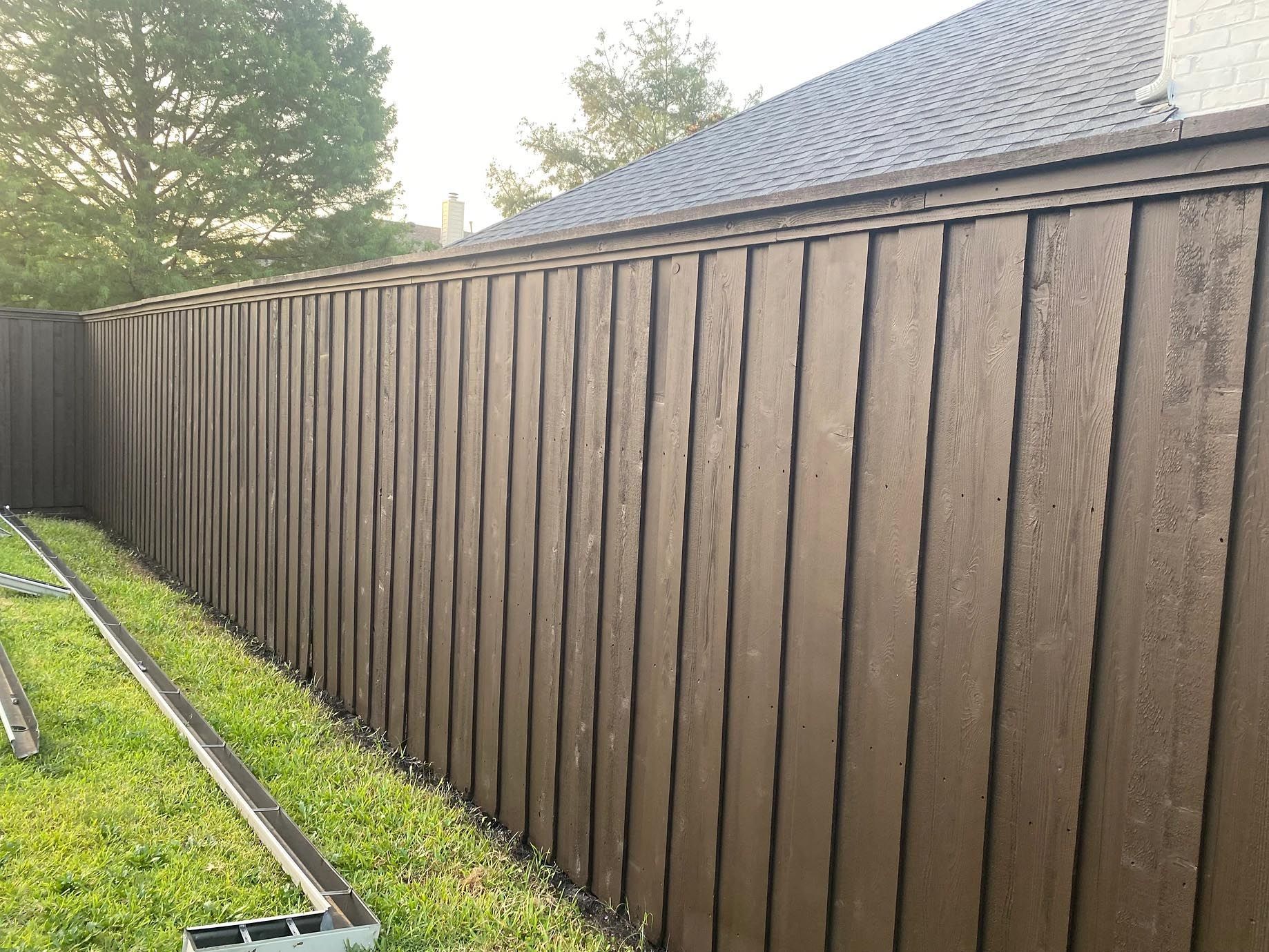 A brown wooden fence is sitting in the grass next to a house.